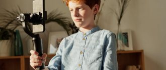 Red-haired boy stands holding a stabilizer with a phone in his hands